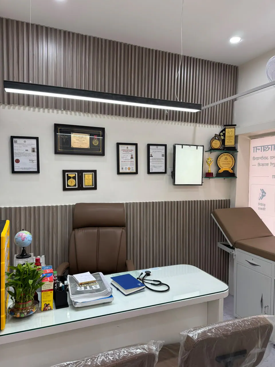 Consultation room with desk, examination couch, and displayed certificates